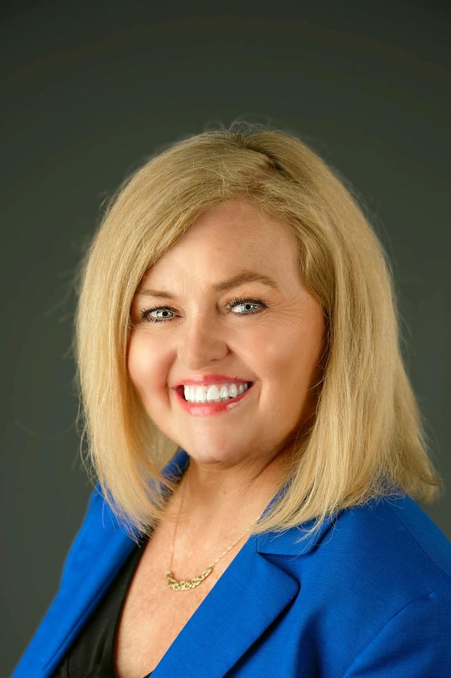 Teresa Kash Davis Portrait with blue and back top and grey background smiling at the camera.