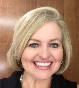 Teresa Kash Davis portrait smiling towards the camera and behind is a wooden background.