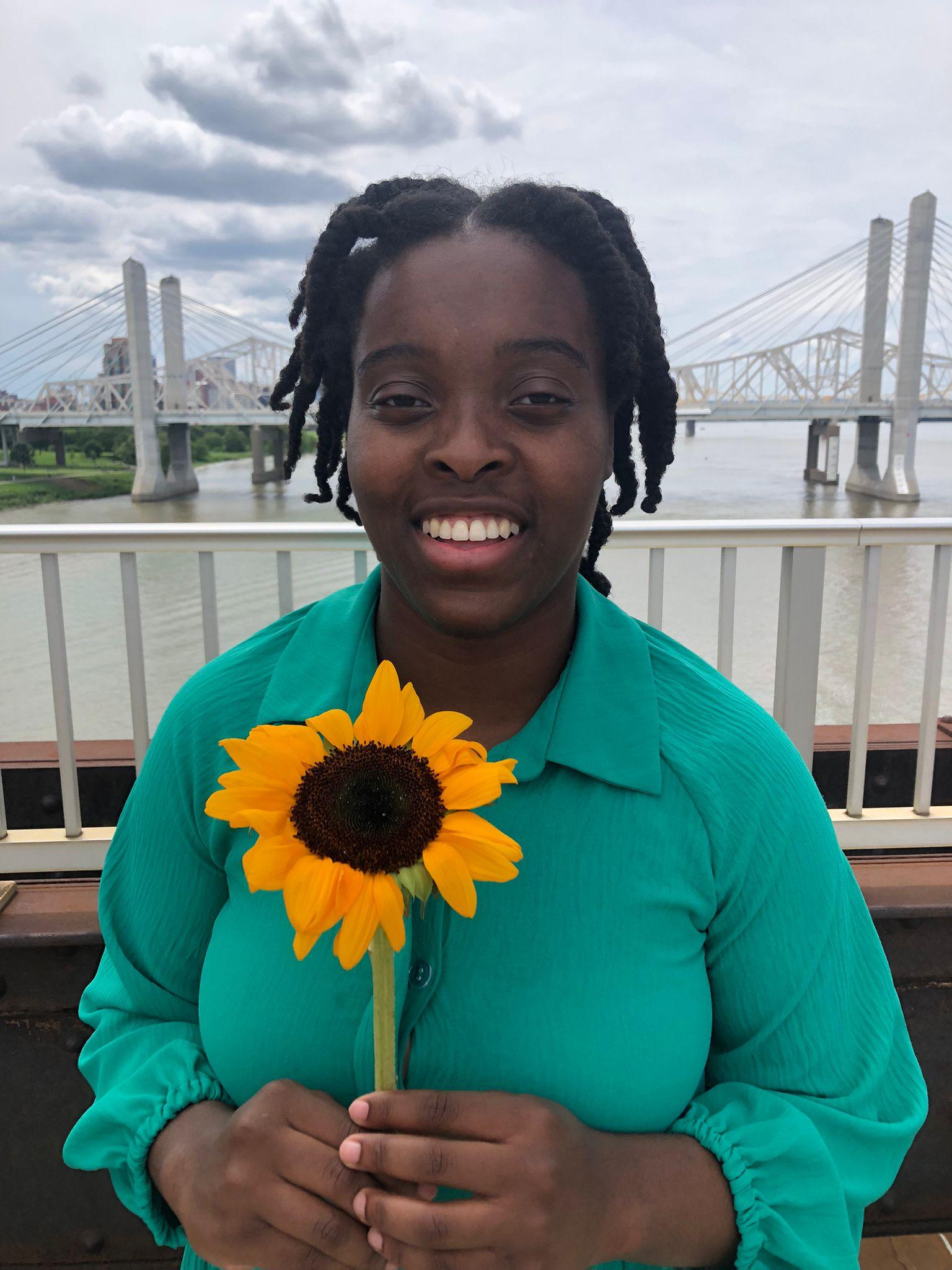 Marlene Michel smiles and holds a felt sunflower